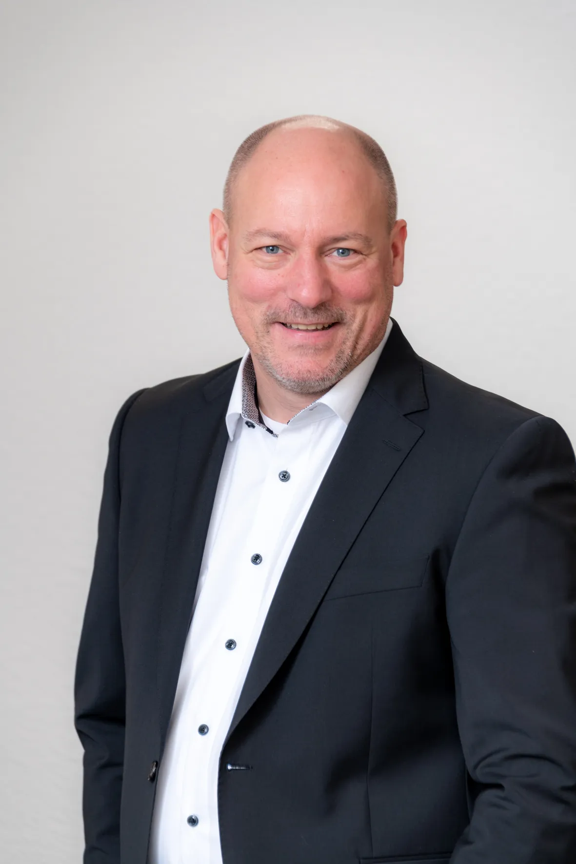 Porträtfoto eines Mitarbeiters der Steuerkanzlei im schwarzen Anzug und weißem Hemd, freundlich lächelnd.