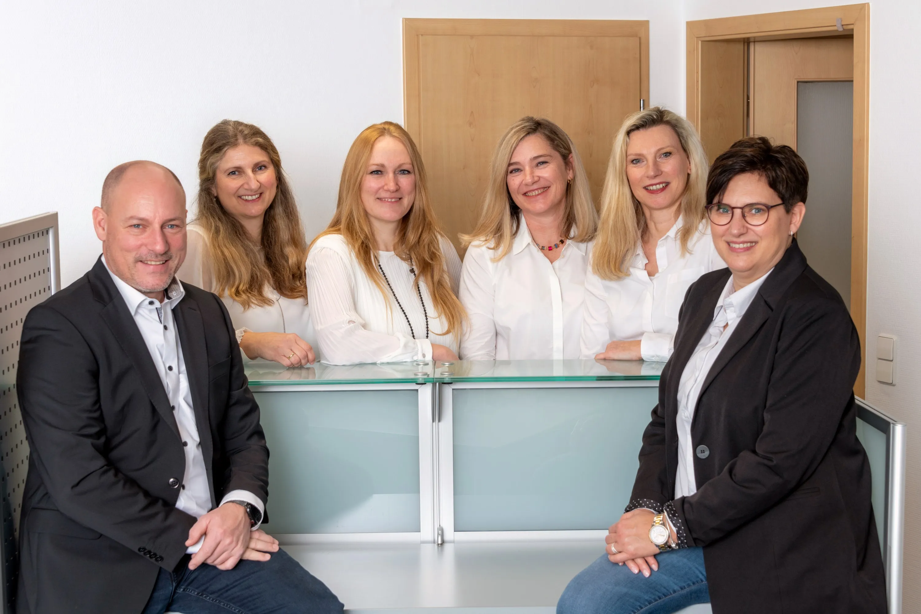 Gruppenfoto des Teams der Steuerkanzlei: Vier Frauen im Hintergrund sowie eine Frau und ein Mann im Vordergrund, alle freundlich lächelnd hinter dem Empfangstresen.