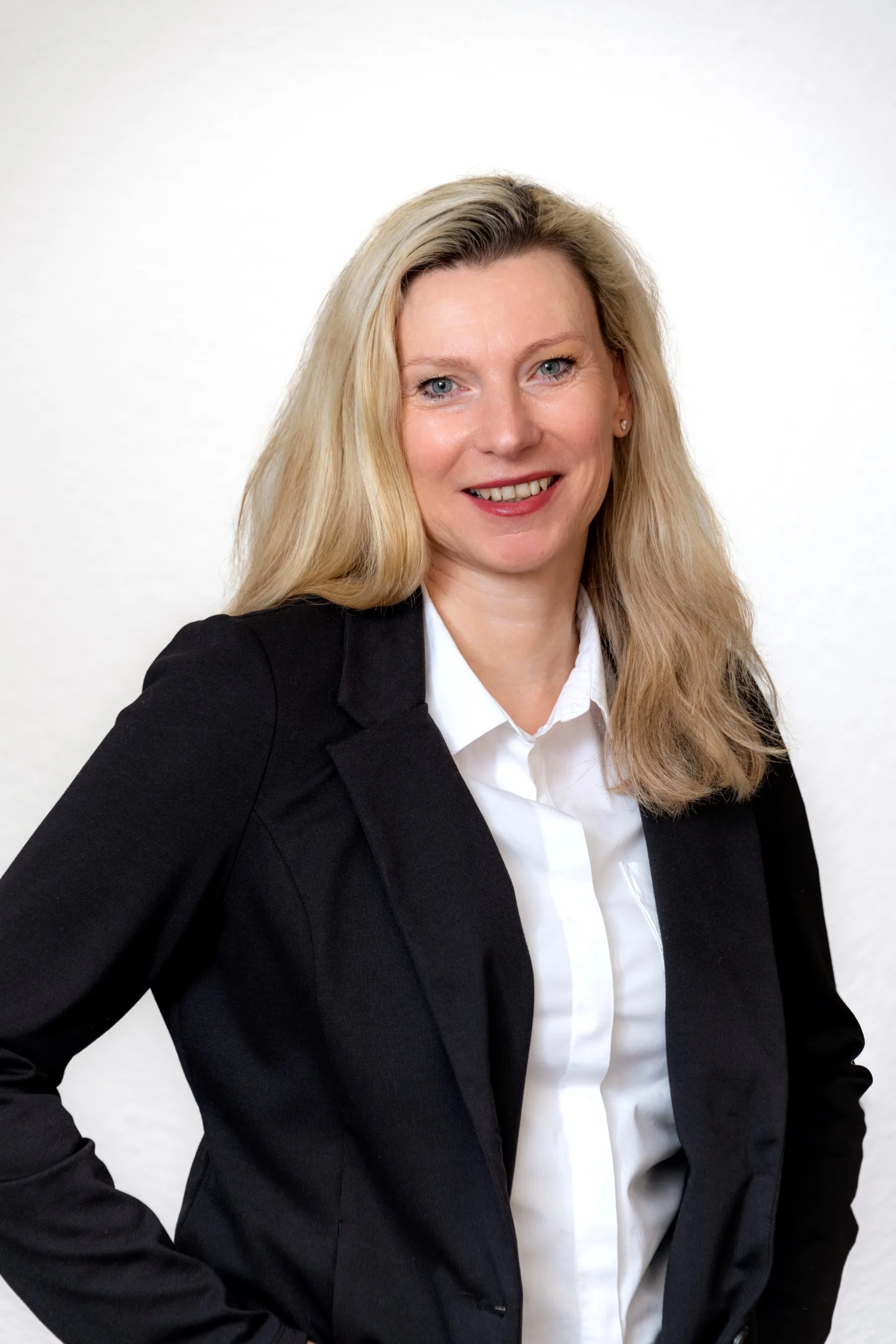 Porträtfoto einer Mitarbeiterin der Steuerkanzlei mit langen blonden Haaren, im schwarzen Blazer und weißer Bluse.