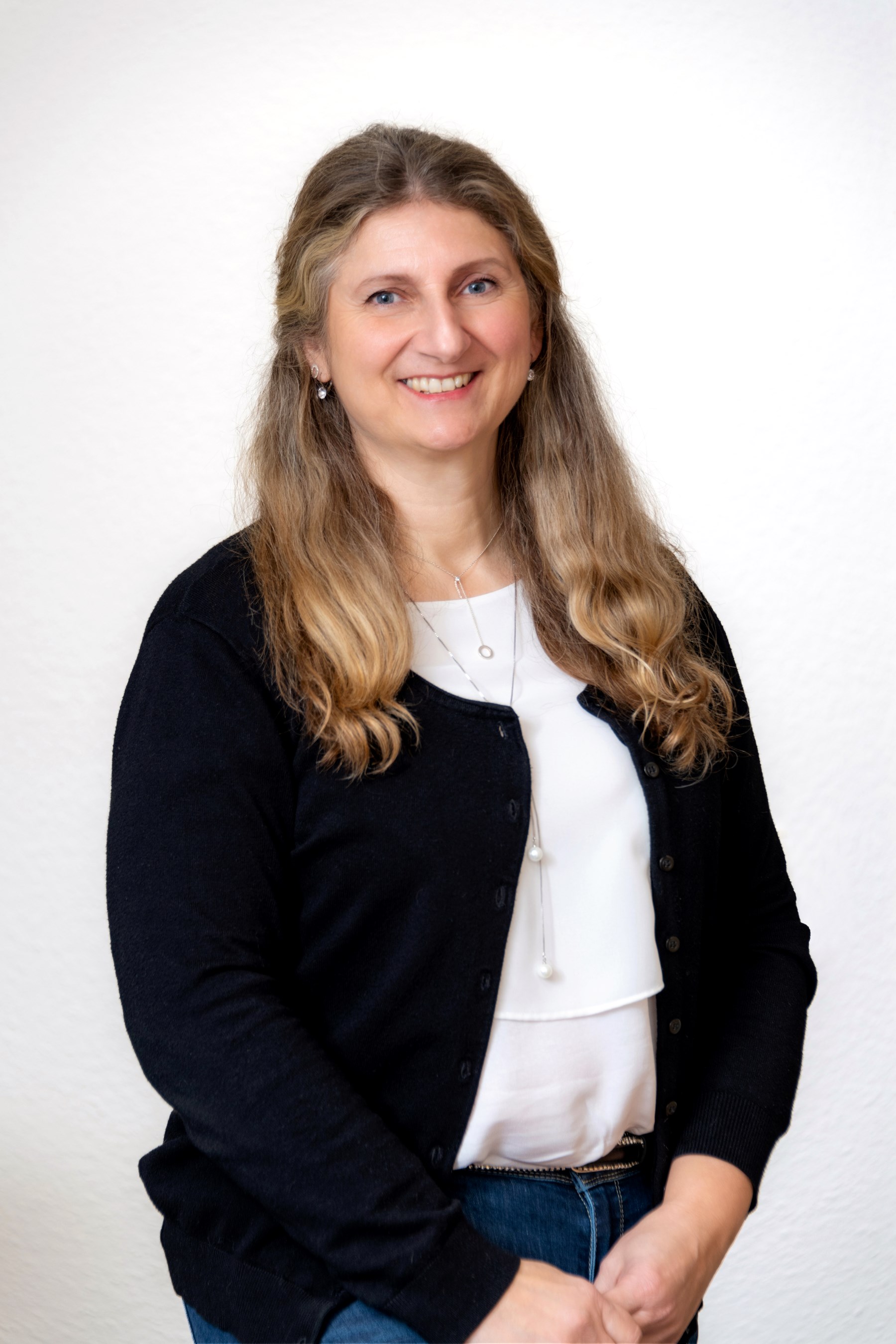 Porträtfoto einer Mitarbeiterin der Steuerkanzlei mit langen lockigen Haaren, im schwarzen Cardigan und weißer Bluse.