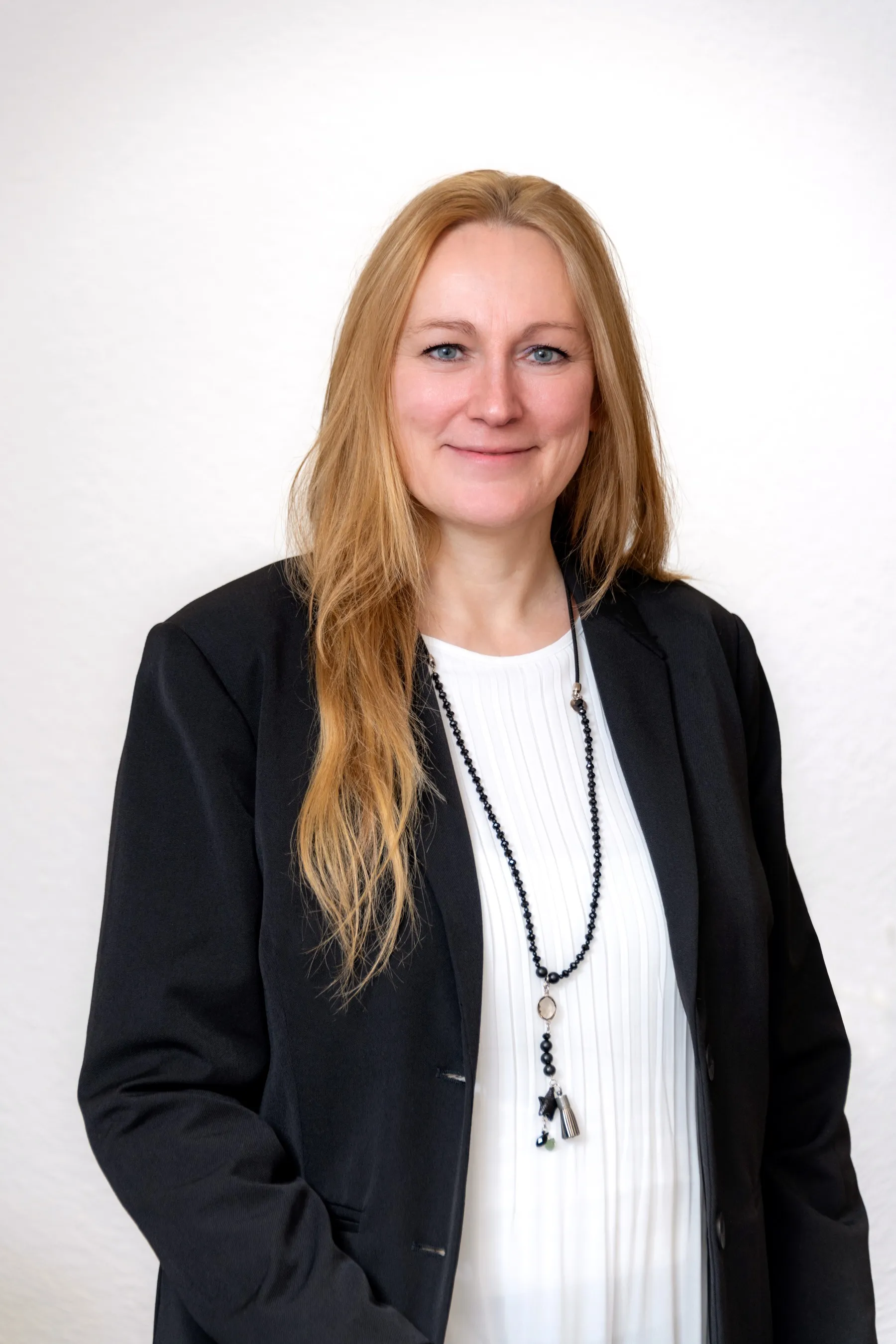 Porträtfoto einer Mitarbeiterin der Steuerkanzlei mit langen blonden Haaren, im schwarzen Blazer und weißer Bluse.