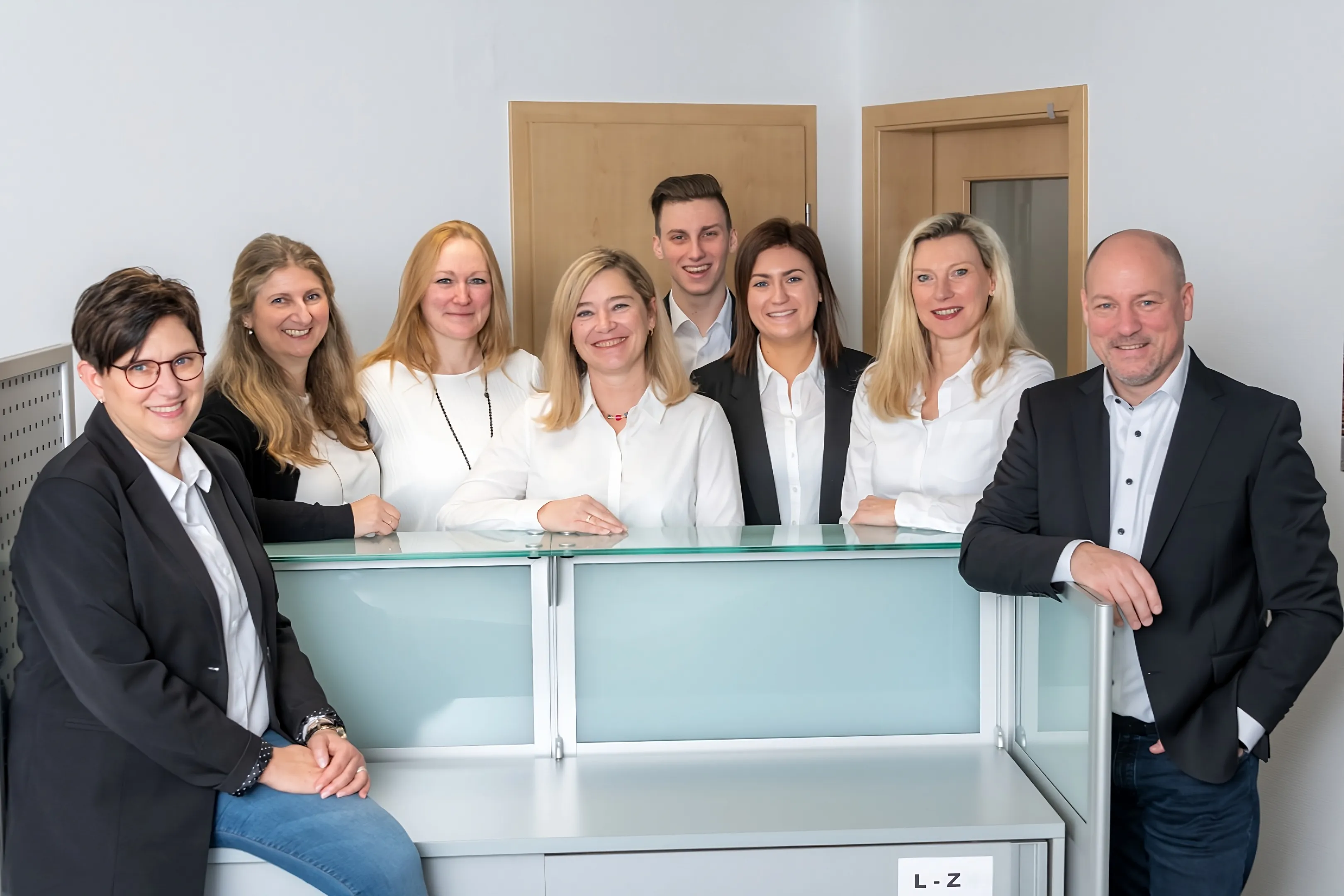 Gruppenfoto des gesamten Teams der Steuerkanzlei: sechs Frauen und zwei Männer – stehen und sitzen freundlich lächelnd hinter dem Empfangstresen.