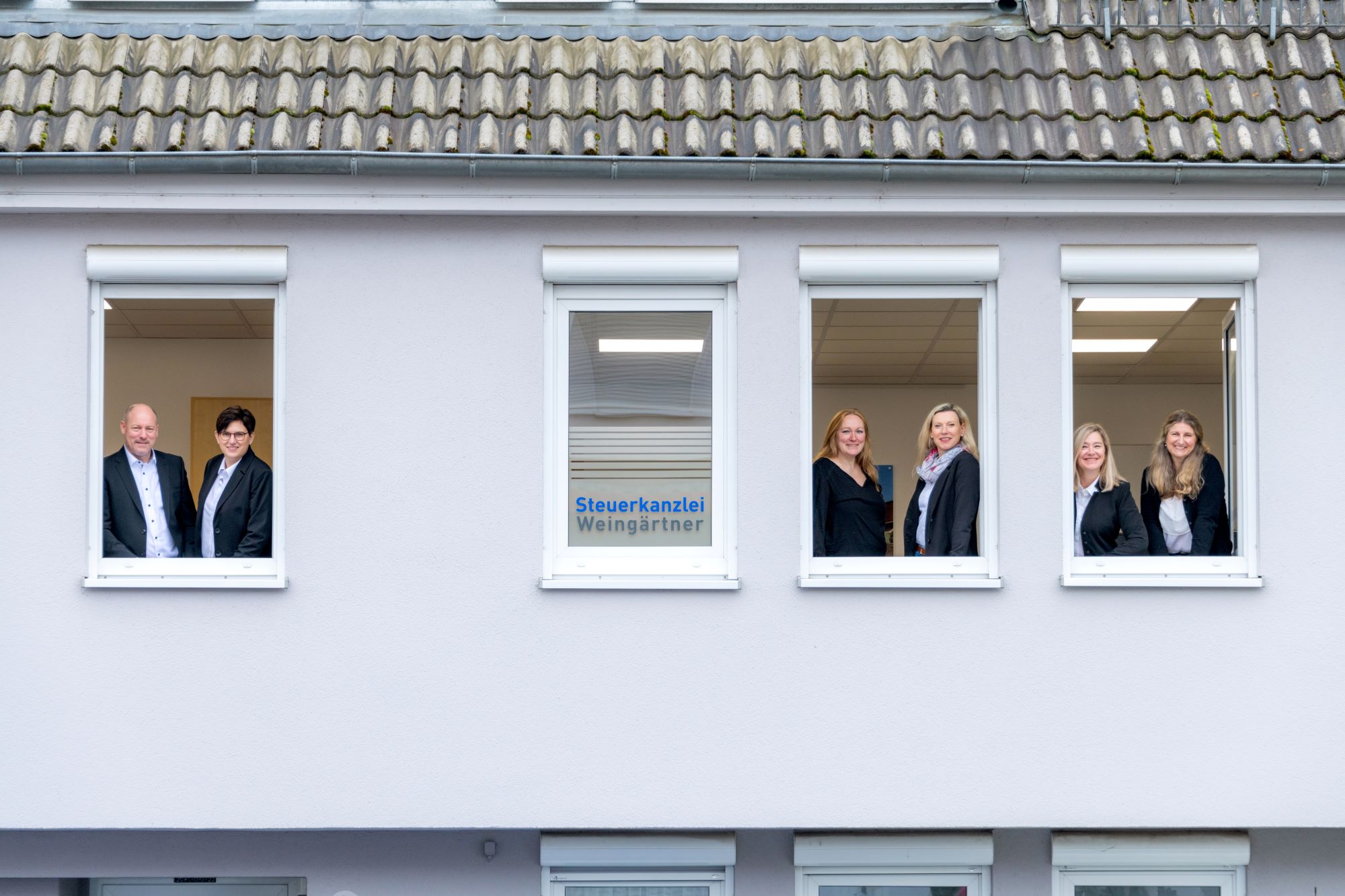 Fassade der Steuerkanzlei Weingärtner mit geöffneten Fenstern, durch die sechs Teammitglieder freundlich herausblicken.
