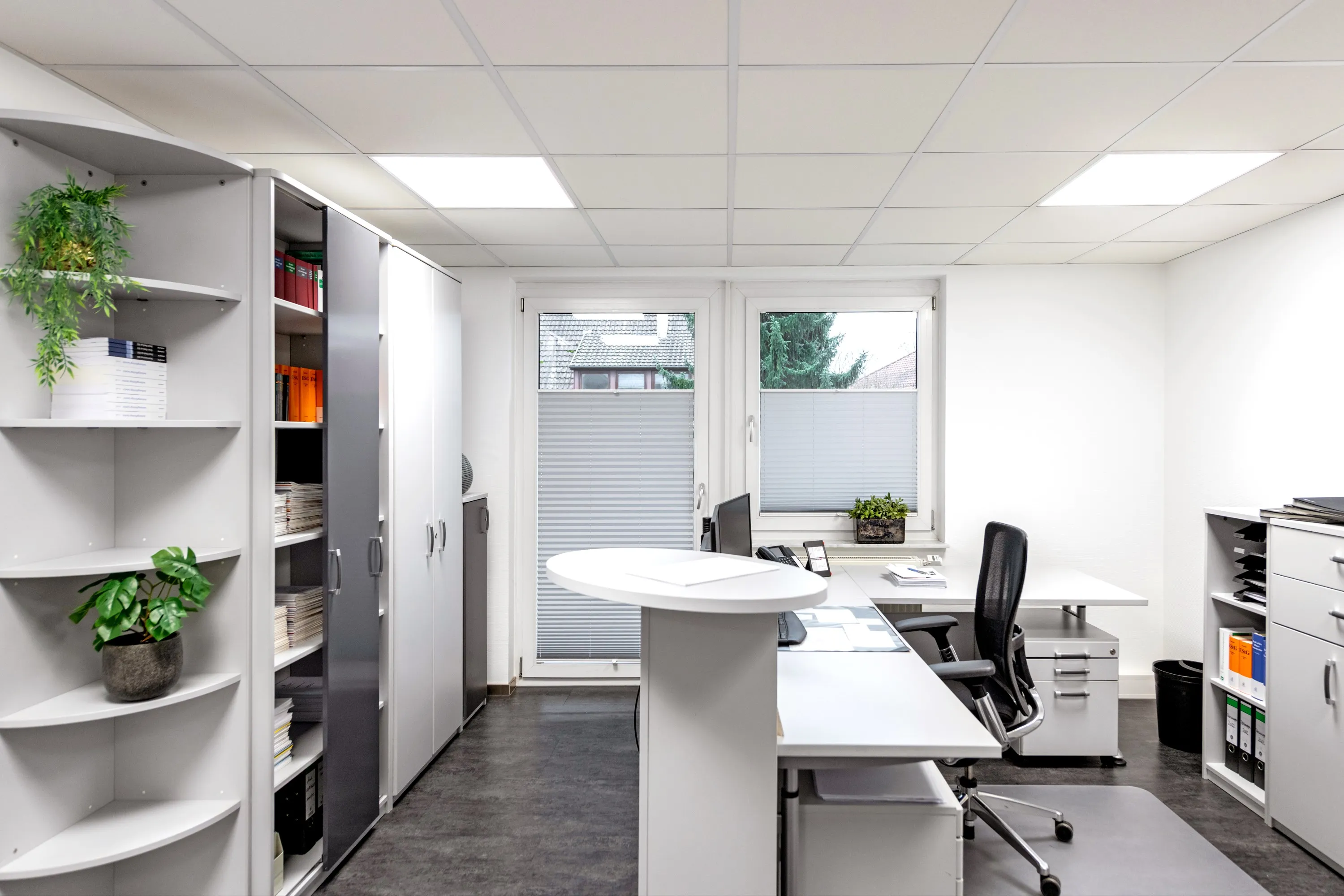 Helles Büro der Steuerkanzlei mit Schreibtischen, ergonomischen Stühlen, Aktenschränken, Regalen und Pflanzen.